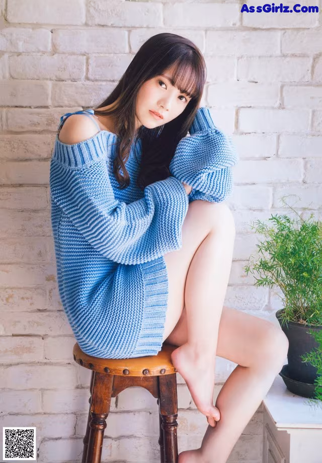 A woman sitting on a stool wearing a blue sweater.