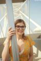 A woman wearing glasses leaning against a pole.