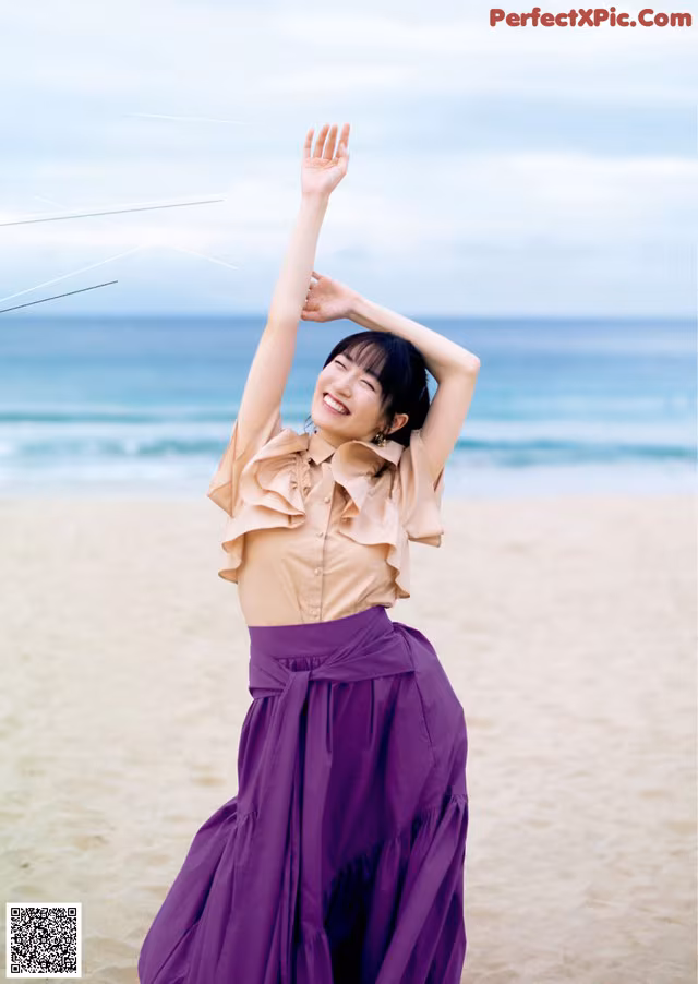 A woman standing on a beach with her arms outstretched.