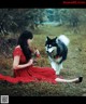 A woman in a red dress sitting in the grass with a dog.