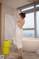 A woman in a white towel standing in a bathroom.