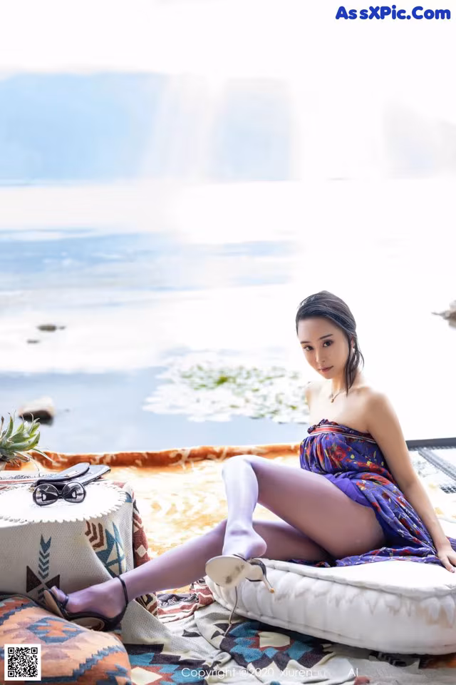 A woman sitting on top of a bed next to a body of water.