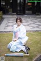 A woman in a blue and pink kimono sitting on the grass.