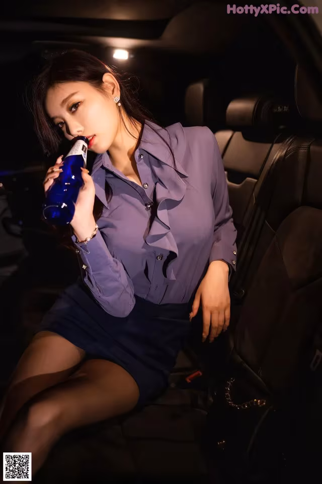 A woman sitting in the back seat of a car drinking from a bottle.