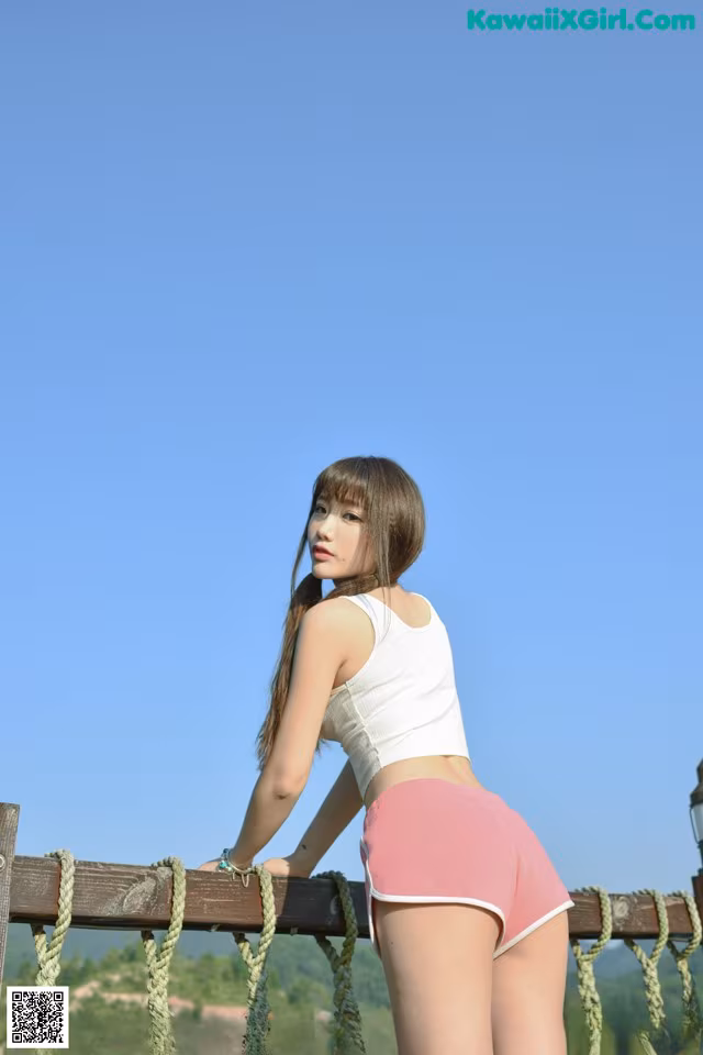 A woman in pink shorts and a white tank top posing on a bridge.