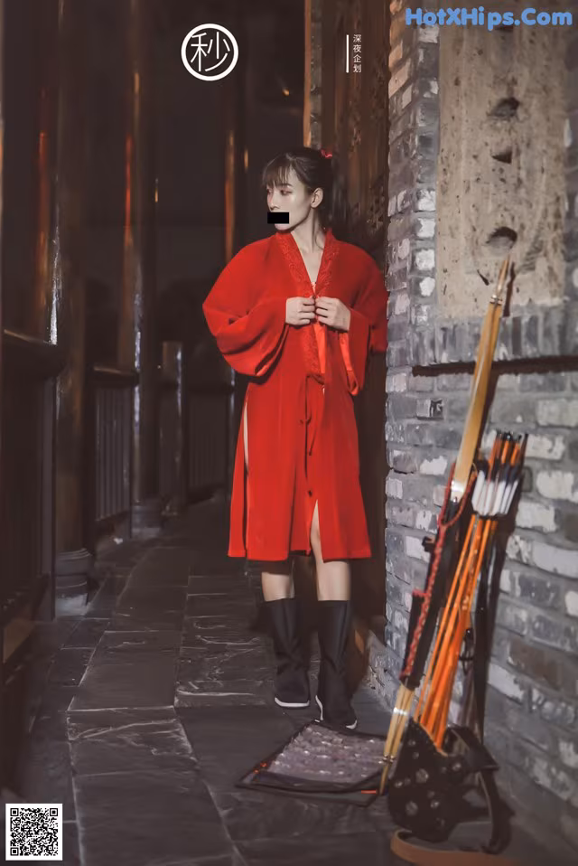 A woman in a red dress standing next to a brick wall.