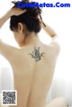 A woman with a tattoo on her back sitting on a bed.