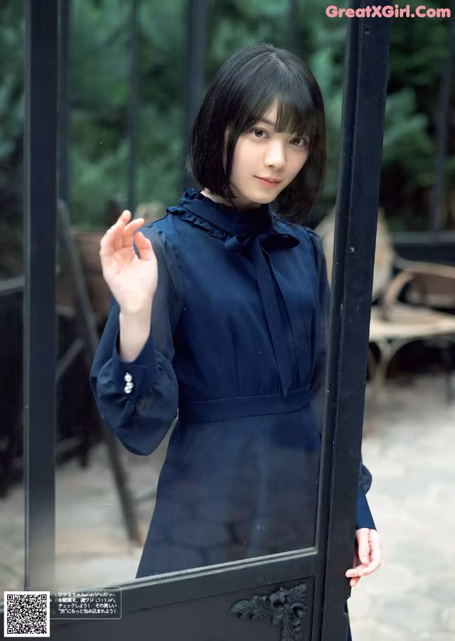 A woman in a blue dress standing in front of a window.