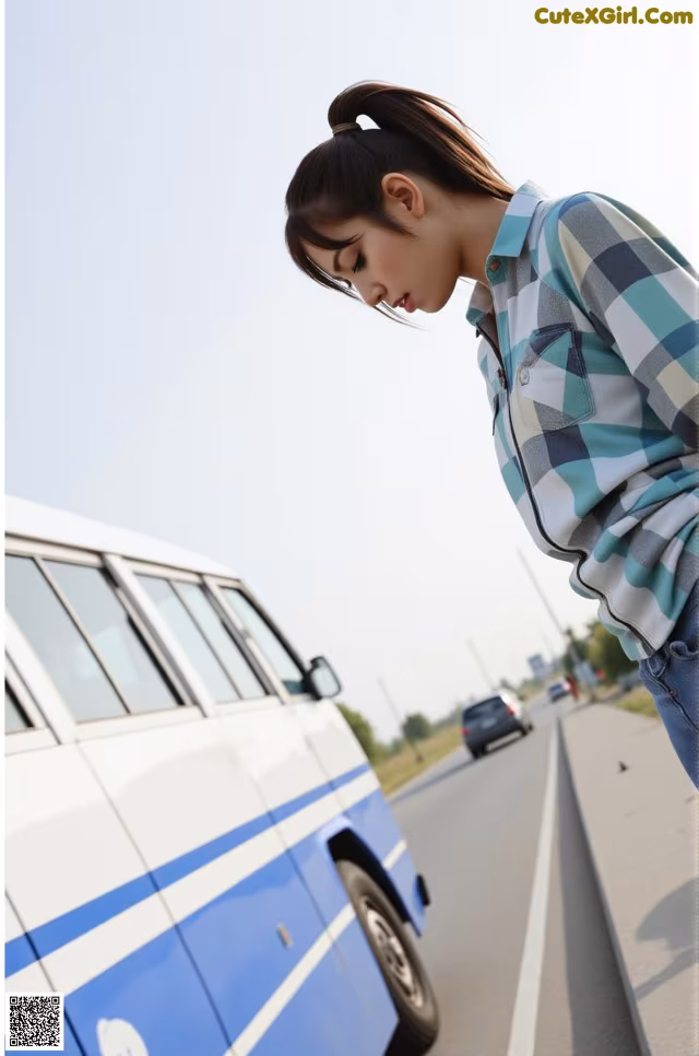 A woman leaning against a blue and white van on the side of the road.